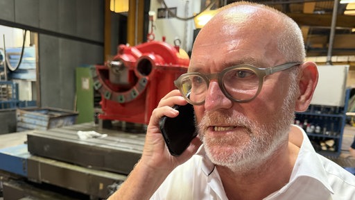 Firmenchef Christian Vogelsang steht in einer Produktionshalle und telefoniert mit einem Handy.