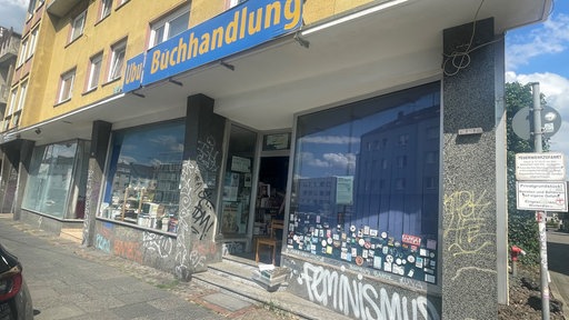 Die Buchhandlung "Ubu" von außen. Eine große Glasfront in der viele bunte Bücher ausgelegt sind.
