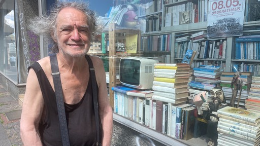 Wolfgang Jöst, ein älterer Mann mit grauen Locken, steht vor seiner Buchandlung.