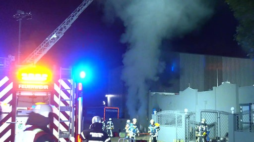 Starker Rauch tritt aus einem Gebäude, Feuerwehrkräfte sind davor mit dem Löschen beschäftigt