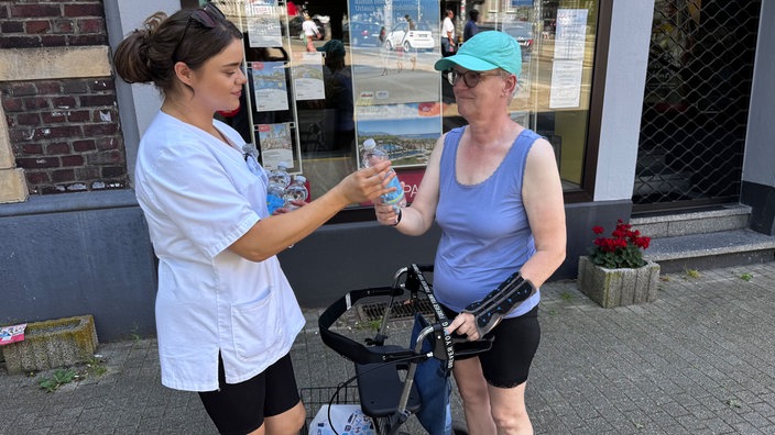 Pflegekraft Joyce verteilt bei Hitze Wasser an Seniorin vor Geschäft in Bochum
