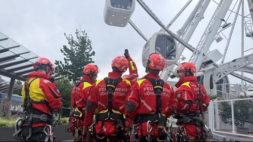 Fünf Einsatzkräfte der Bochumer Höhenrettung stehen vor dem Riesenrad im Ruhr Park und schauen nach oben