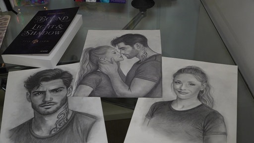 Drei Bleistift-Zeichnungen auf einem Tisch, auf einer küssen sich ein Mann und eine Frau, die anderen sind Portrait-Aufnahmen der Frau und des Mannes