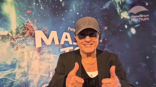 Peter Schilling mit zwei Daumen hoch vor einem Plakat im Planetarium