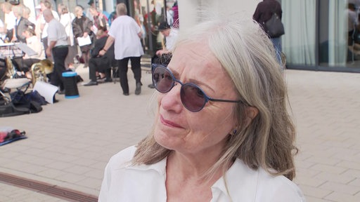 Eine Frau mit weißer Bluse und Sonnenbrille steht vor der Vonovia-Zentrale, im Hintergrund links sind Musiker mit ihren Instrumenten zu sehen