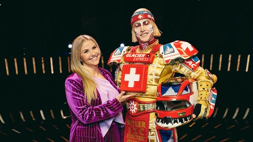 Sängerin Beatrice Egli in einem lilafarbenen Anzug steht neben Musicaldarsteller René Lohse in seiner Rolle als Ticktack, der neuen "Starlight Express"-Figur, auf der Bühne des Musicals in Bochum.
