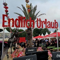 Über Bierbänken und zwischen Festivalzelten steht ein Banner mit der Aufschrift "Endlich Urlaub" 