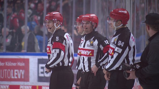 Andre Schrader steht im Schiri-Trikot auf dem Eis. HInter ihm stehen 3 weitere Männer im Schiri-Trikot.