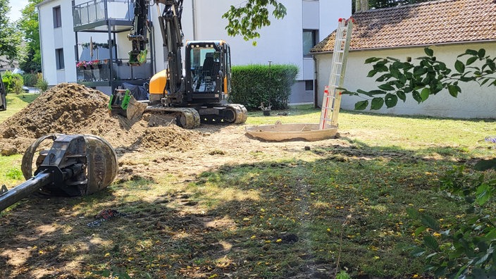 Ein kleiner Bagger steht vor einem gegrabenen Loch
