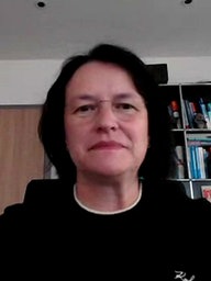 Eine Frau mit dunklen Haaren sitzt vor einem Bücherregal