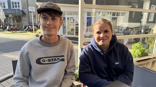Damian und Clara sitzen draußen an einem Tisch.