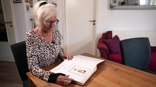 Erika Schneider sitzt an einem Tisch, vor ihr liegt ein Fotoalbum.