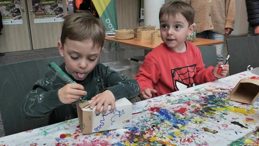 Zwei Kinder an einem Tisch, sie bemalen Kartons