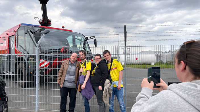 Vier Menschen stehen vor einem Löschfahrzeug am Dortmunder Flughafen.