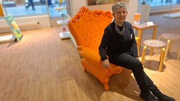 Künstlerin Helga Hoicke sitzt in der Pop-Up Galerie im ehemaligen Kaufhof in Dortmund auf einem orangenen Sessel