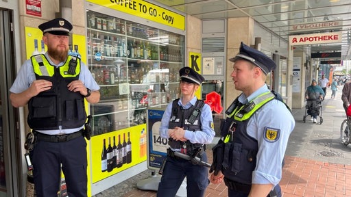 Das Bild zeigt drei Mitarbeitende der Stadt vor einem Geschäft stehen
