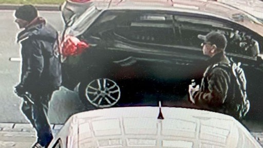 Zwei dunkel gekleidete Männer, die auf dem Bürgersteig vor einem Auto laufen