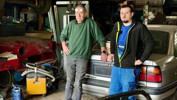 Achim und Andreas Hildebrand stehen in einer Werkstatt vor einem Auto.