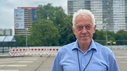Ein Mann in einem blauen Hemd steht vor zweu Hochhäusern