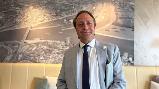 Willem Hamer, Hoteldirektor vom Hotel Rheingarten in Homberg, trägt einen grauen Anzug und eine dunkelblaue Krawatte.