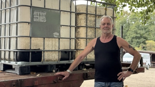 Ein Mann mit einem schwarzen Oberteil steht vor zwei großen Wassercontainern