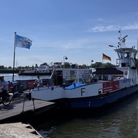 Eine Fähre steht im Wasser an einem Anleger. Zwei Personen verlassen die Fähre auf Fahrrädern