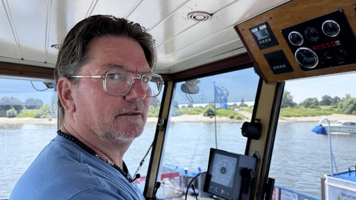 Ein Mann steht im Fahrerhäuschen eines Boots was über den Rhein fährt