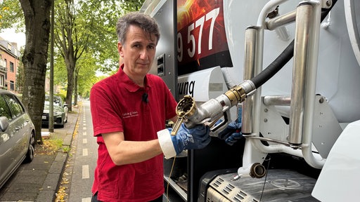 Ein Mann mit dunklen, leicht grauen Haaren und rotem Poloshirt steht an einem Tankwagen und hält einen Schlauch in der Hand