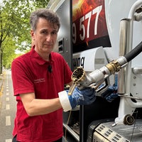Ein Mann mit dunklen, leicht grauen Haaren und rotem Poloshirt steht an einem Tankwagen und hält einen Schlauch in der Hand