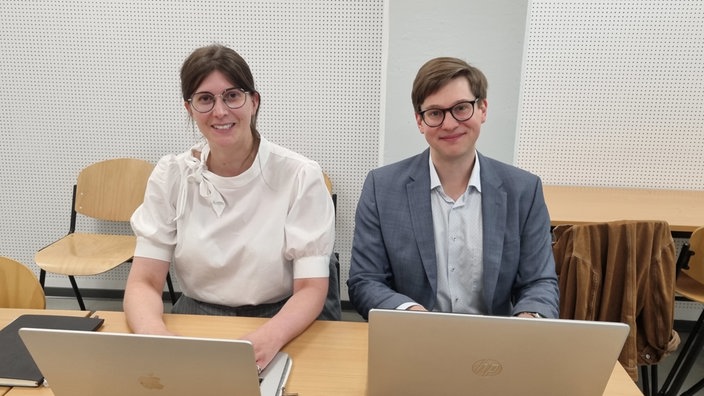Ein Frau und ein Mann, Carmen Behrendt und Helge-Fabien Hertz, sitzen an Schreibtisch 