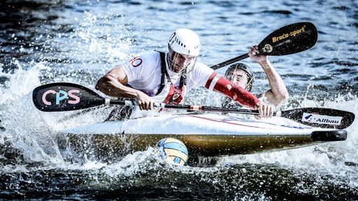 Zwei Kanufahrer kämpfen im aufgepeitschten Wasser um den Ball