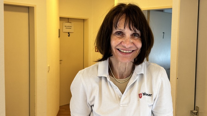Dr. Anne Rauhut lächelt in die Kamera. Sie hat einen schwarzen Bob und trägt ein weißes Hemd mit dem Logo der Malteser.