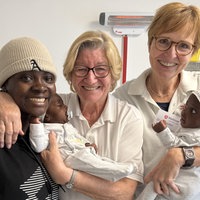 Dr. Delia Streuter und Hebamme Doris Kammann mit ihrer früheren Patientin Mariama. Die drei Frauen lächeln in die Kamera und halten zwei Babys.