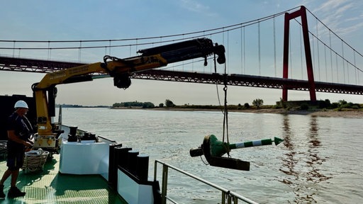 Markierungstonne wird mithilfe eines Krans auf einem Boot ins Wasser gesetzt