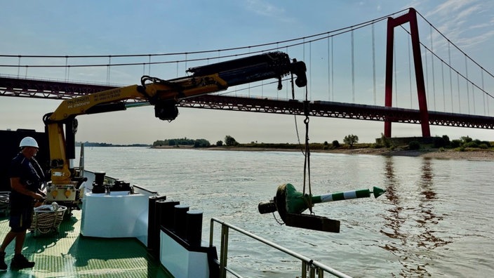 Markierungstonne wird mithilfe eines Krans auf einem Boot ins Wasser gesetzt