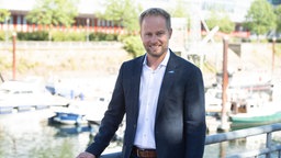 Ein Mann in Anzug steht lächelnd am Hafenbecken des Innenhafens in Duisburg