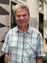 Ein Mann mit grauen Haaren und grau-weiß-blau karriertem Hemd lächelt in die Kamera