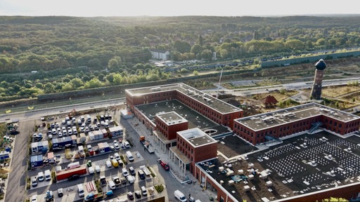 Ein großes Gebäude, ein Turm, ein Parkplatz und ein Wald im Hintergrund