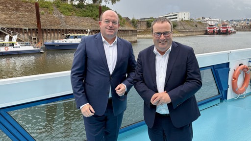 Zwei Männer, links Hafenchef Bangen und rechts NRW-Minister Krischer, stehen in blauen Anzügen auf einer Fähre