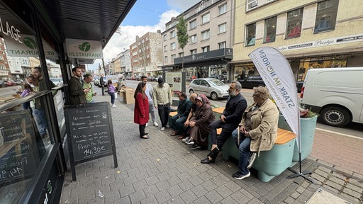 Mehrere Fußgänger entspannen sich vor dem Café auf den neuen Sitzgelegenheiten