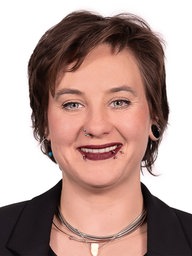 Eine junge Frau mit kurzen braunen Haaren und einigen Piercings im Gesicht lächelt in die Kamera