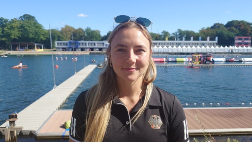Eine blonde Frau mit Sonnenbrille auf dem Kopf und schwarzen Oberteil guckt in die Kamera