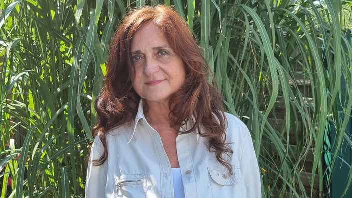 Regina Basic heute, mit offenen Haaren im sonnigen Garten