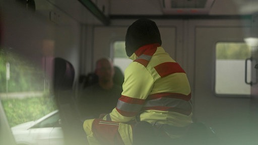 Ein Mann in Rettungsdienst-Kleidung von hinten, anonymisiert, in einem Krankenwagen.