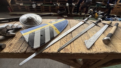Abgestumpfte Schwerter und Schilder liegen auf einem Holztisch
