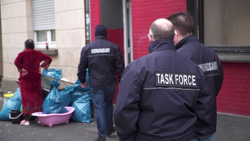 Männer von hinten mit blauen Uniformen, auf denen "Taskforce" oder "Ordnungsamt" steht