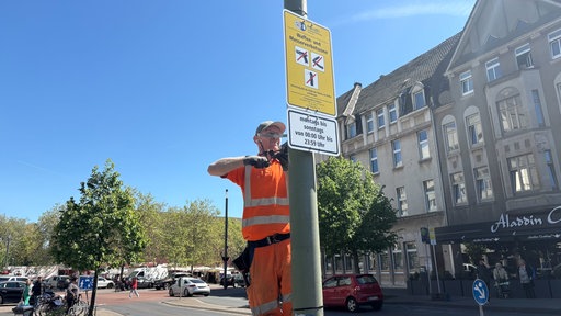 Bauarbeiter bohrt mit einer Bohrmaschine Schilder an einen Pfahl, die das Gebiet als Waffenverbotszone kennzeichnen.