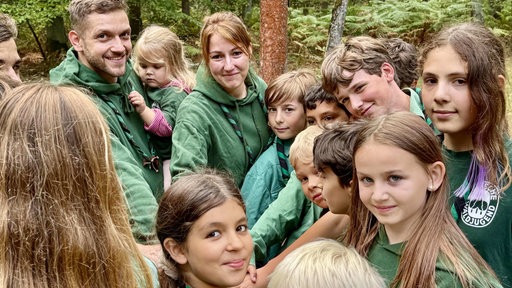 Kinder und Erwachsene der Waldjugend Duisburg tragen grüne Kapuzenpullis im Wald.