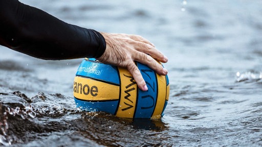 Eine Hand greift nach einem Ball im Wasser