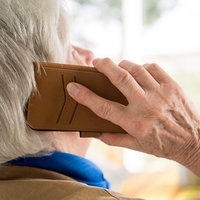 Eine Frau mit grauen Haaren ist von hinten zu sehen, sie hält ein Telefon ans Ohr